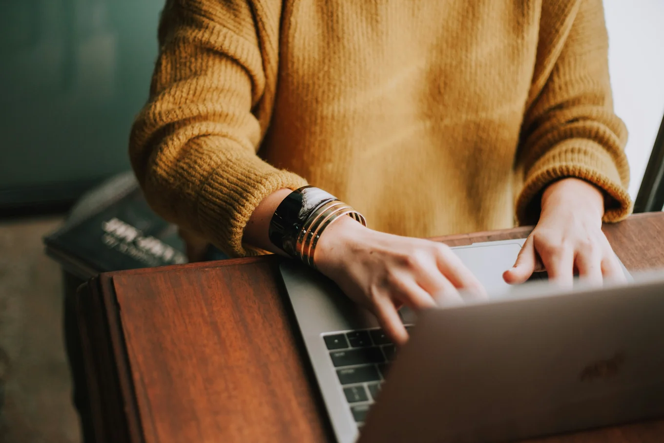 The torso of a person in a mustard coloured jumper tapping on a keyboard.